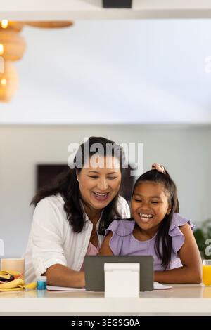 Afroamerikanische Mutter in weißem Hemd und Jugendtochter lacht mit Tablette an der Theke Stockfoto