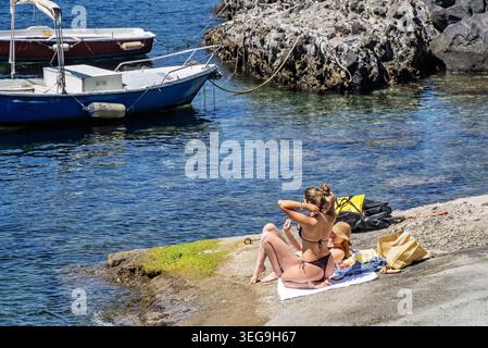 Zwei schöne junge Frauen in Bikinis, die sich auf einer Wasserrutsche neben dem Schloss Aragonese, IOschia, Italien auf 2 M<AY 2026 sonnen Stockfoto