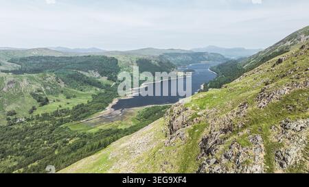 Ein atemberaubender Panoramablick fängt die Weite eines Tals mit einem dunkelblauen See, dichten Wäldern und zerklüfteten Hügeln unter klarem Himmel ein Stockfoto