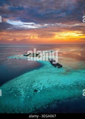 Eine wunderschöne paradiesische Insel auf den Malediven mit Wasserbungalows über dem türkisfarbenen Meer mit leuchtenden Korallenriffen während eines dramatischen Sonnenuntergangs Stockfoto