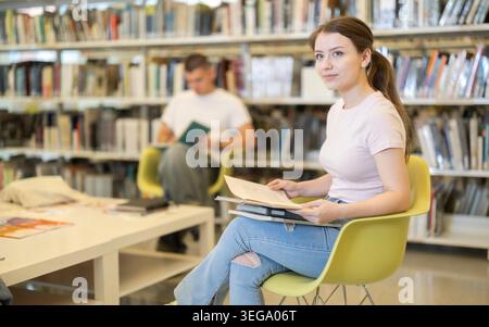 Frau sitzt auf einem Stuhl in der Bibliothek vor dem Hintergrund von Studenten Stockfoto
