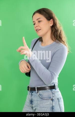 Junge Frau, die einen virtuellen Bildschirm vor dem grünen Bildschirm benutzt Stockfoto