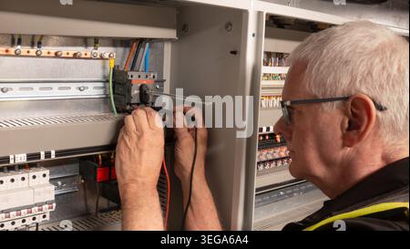 Leitender Elektroingenieur, der ein Multimeter zur Prüfung eines Trennschalters an einem Gebäudemanagementsystem verwendet. Ausgereifte Inspektionen von Elektrofachfirmen Stockfoto