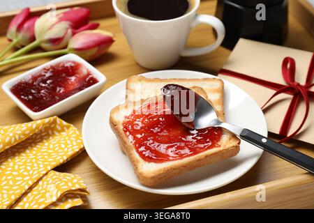 Holztablett mit leckerem Frühstück, Umschlag und Tulpenblumen auf dem Tisch, Nahaufnahme Stockfoto
