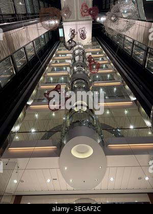 Blick geradeaus auf einen vertikalen Glasaufzugsschacht in einer modernen großen Kreuzfahrtschiff-Atrium-Lobby. Stockfoto