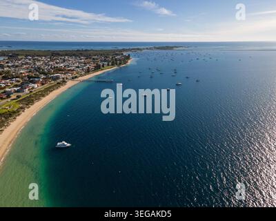 Dieses atemberaubende Luftbild fängt eine malerische Küstenstadt ein, eingebettet in das azurblaue Wasser des Ozeans. Die Szene zeigt einen ruhigen Strand gesäumt von Stockfoto