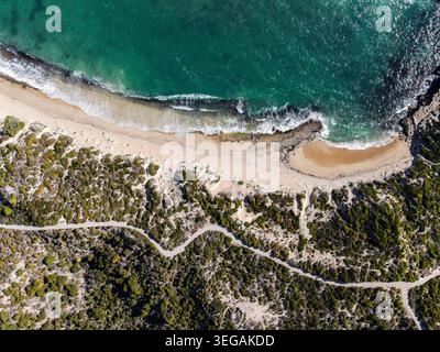 Dieses atemberaubende Luftbild fängt eine ruhige Küstenlandschaft mit einem unberührten Strand ein, der von üppigem Grün und sanften Wellen umgeben ist Stockfoto