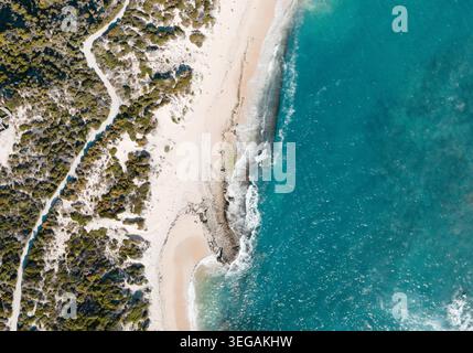 Dieses atemberaubende Luftbild fängt eine ruhige Küstenlandschaft mit einem unberührten Strand mit goldenem Sand und klarem türkisfarbenem Wasser sanft la ein Stockfoto