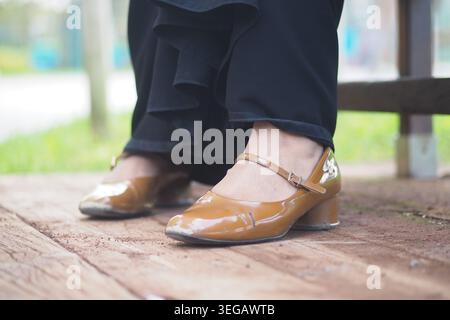 Frau mit braunen Schuhen sitzt draußen auf einer Holzbank Stockfoto