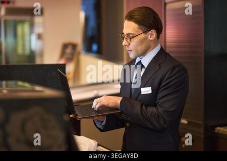 Erwachsener Hotelrezeptionist arbeitet am Laptop während des Check-ins der Gäste Stockfoto