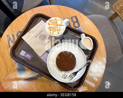 Johor, Malaysia, 13. Mai 2026: Blick von oben auf Cappuccino mit Karamell-Nieseln, Tiramisu-Dessert und Creme-Krug auf Café-Tablett. Stockfoto