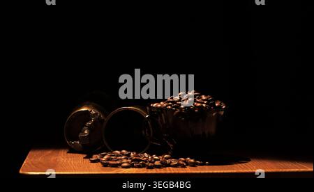 Ganze Kaffeebohnen, die aus einem manuellen Mahlwerk ausgeschüttet werden und eine Keramikschale füllen, betonen das Morgenritual und die satten dunklen Töne des gerösteten Kaffees Stockfoto