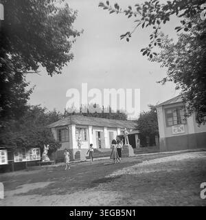 Sloviansk, 1983, Slavkurort, Pionierlager Wishnegorsk. Mehrere Kinder laufen und spielen im sonnigen Innenhof zwischen den einstöckigen Wohnhäusern des Sommercamps. Der Außenbereich ist mit klassischen sowjetischen Gipsskulpturen von Pionieren und Athleten dekoriert, umgeben von Bäumen. Ein historisches Schwarzweiß-Archivfoto, das die authentische Atmosphäre der Epoche, den architektonischen Stil der Jugendeinrichtungen und den friedlichen Donbass feststellt. Stockfoto