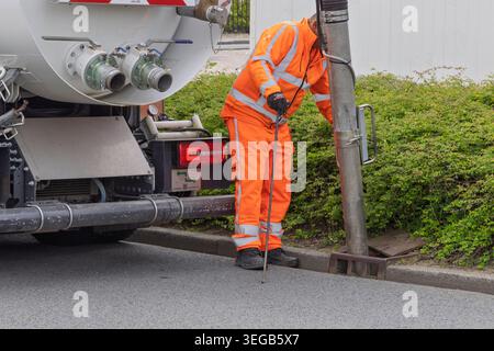Leiden, Niederlande, 08. Mai 2026. Nahaufnahme eines Arbeiters in orangefarbener Sicherheitsausrüstung, der einen Straßenrinnenablauf mit einem Vakuumrohr reinigt. Stockfoto