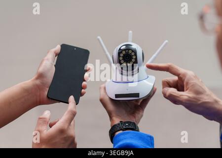 Asiatische Männer, die eine intelligente Heimkamera mit Smartphone einrichten Stockfoto