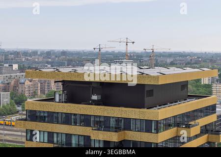 Amsterdam, Niederlande, 08. Mai 2026. Photovoltaik-Solarpaneele, die auf dem Dach eines modernen hohen Gebäudes mit Goldakzenten installiert sind. Stockfoto