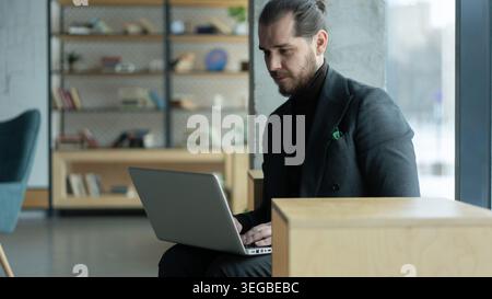 Portrait-Geschäftsmann mit Laptop-Computer, der in modernen Büros arbeitet. Ein lächelnder, gutaussehender Unternehmer im mittleren Alter Stockfoto