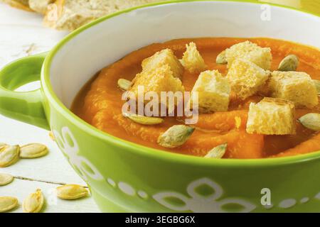 Kürbis Squash Gemüsesuppe mit Croutons und Kürbiskerne in einer grünen Schale auf weißem Hintergrund aus Holz, Nahaufnahme Stockfoto