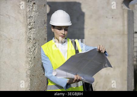 Architektin mit Sicherheitsweste und Schutzhelm, die die Baupläne auf einer Baustelle überprüft Stockfoto