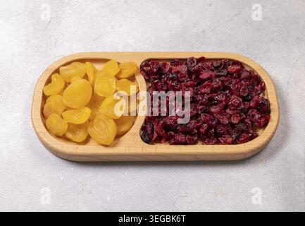 Getrocknete Aprikosen und Preiselbeeren, die gesunde und nahrhafte Snacks bieten, sind ordentlich auf einem Serviertablett aus natürlichem Holz gegen einen hellgrauen bac angeordnet Stockfoto