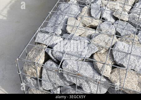 Detail einer Gabionenwand aus Granitsteinen und Drahtgeflecht für Landschaftsgestaltung Stockfoto
