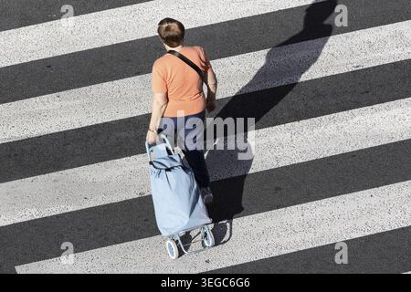 Eine nicht erkennbare Seniorin zieht an einem sonnigen Tag einen Einkaufswagen über einen Quersteg. Hochwinkelansicht Stockfoto