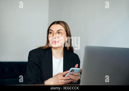 Attraktive Frau mit Smartphone und Blick auf den Schreibtisch. Unternehmen. Büroarbeit. Weibliche professionelle Kommunikation. Beauty-Porträt. Corpo Stockfoto