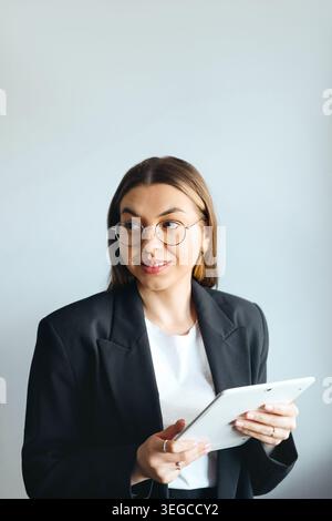 Hübsche Frau, die ein Tablet hält und im Büro lächelt. Unternehmen. Büroarbeit. Frau, die ein Tablet verwendet und kommuniziert. Beauty-Porträt. Korpora Stockfoto