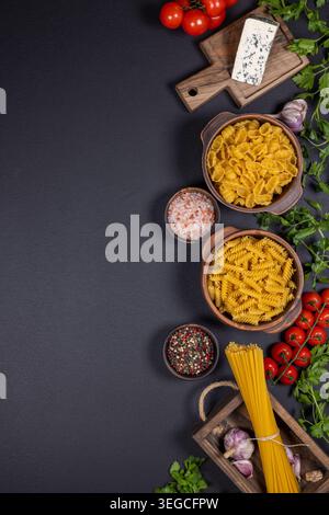 Verschiedene rohe Nudelsorten mit Reifen Kirschtomaten. Frische Petersilie. Knoblauch. Blauschimmelkäse. Und verschiedene Gewürze in kleinen Schüsseln. Alle auf einem angeordnet Stockfoto