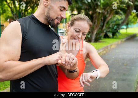 Fitnesspaar überprüft die Smartwatch während des Workouts im Tropical Park Stockfoto
