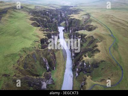 Blick aus der Vogelperspektive auf den Fjadrargljufur Canyon mit seinen steilen moosigen Klippen und dem gewundenen Fluss Fjadra, der durch das Tal Skaftarhreppur, Island fließt. Stockfoto