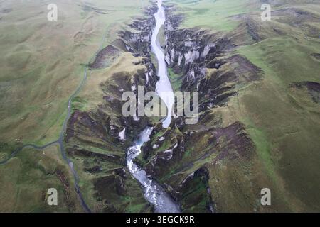Aus der Vogelperspektive auf den Fjadrargljufur Canyon mit seinem gewundenen Fluss und steilen moosbedeckten Klippen unter dem nebeligen Himmel Skaftarhreppur, Island. Stockfoto