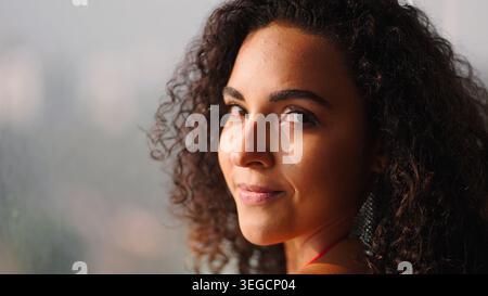 Eine junge Frau mit schönen lockigen Haaren, die lächelnd in die Kamera blickt Stockfoto