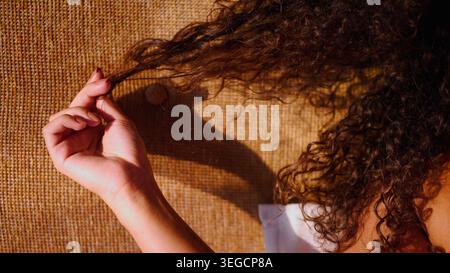Die Hand der Frau zieht an lockigen braunen Haaren und zeigt eine natürliche Selbstpflegestruktur Stockfoto