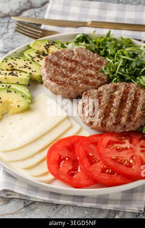 Keto Burger Teller mit Käse, Avocado, gegrilltem Patty und Tomaten aus nächster Nähe auf dem Tisch. Vertikal Stockfoto