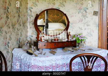 Antiker Antik-Holzkommode mit einem Vintage-silbernen Kosmetiktisch auf einer weißen Tischdecke aus Spitze vor einer floralen Chintztapete. Stockfoto