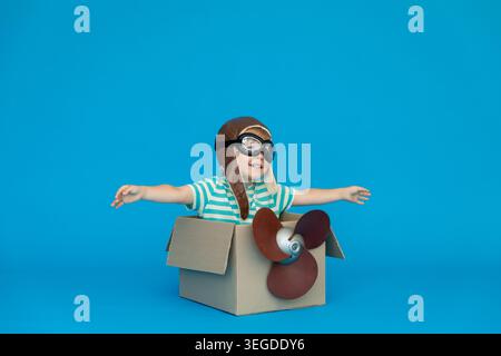 Glückliches Kind träumt davon, Pilot zu werden. Junge, der Spaß vor blauem Papier hat. Junge mit gestreiftem Hemd, der in Pappkarton spielt. Sommerurlaub Stockfoto