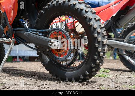 Nahaufnahme eines hinteren geknöpften Reifens, eines orangefarbenen hinteren Kettenrads und einer Antriebskette auf einem Geländemotocross-Motorrad im Freien. Detailansicht eines Dirt Bike hinten wh Stockfoto
