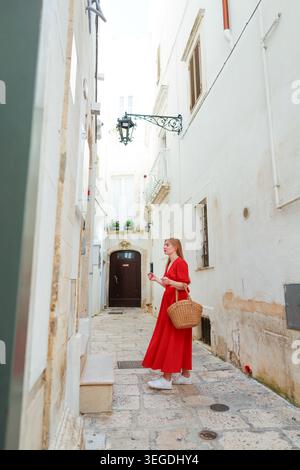 Frau, die die sonnige europäische Altstadt in rotem Kleid genießt, die Luxusurlaub und romantische Reisemelosigkeit einfängt. Stockfoto