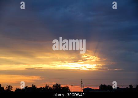 Dramatische Sonnenstrahlen, die bei Sonnenuntergang durch dunkle Wolken brechen. Stockfoto