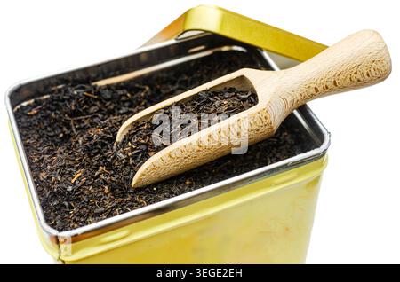 Hochwinkel-Makroaufnahme aus hochwertigem schwarzem Tee mit losem Blatt, der einen alten gelben Blechbehälter mit traditionellem Messschaufel aus Holz füllt Stockfoto