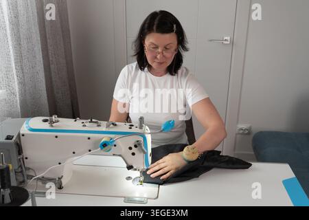 Nahaufnahme von Frauen, die mit Nähmaschine Stoff nähen, während der Bekleidungserstellung und Schneiderei. Detaillierte Textilarbeit mit Nähten, Fäden und en Stockfoto