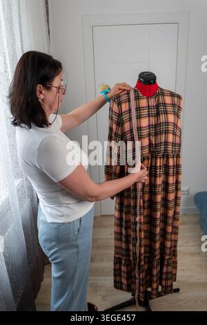 Vertikalansicht einer Frau, die während der Schneiderei und des Nähprozesses im Atelier Messungen an einer professionellen Schneiderpuppe durchführt. Modedesigner arbeitet Stockfoto