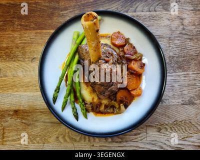 Lammkeule mit Kartoffelpüree und gedämpftem Spargel. Geschmorte Lammkeule mit Rotwein, Karotten, Selleriestangen, Zwiebeln, Knoblauch, Tomaten, Kräuter, Gewürze Stockfoto