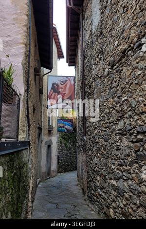 Cannero Riviera, Lago Maggiore, Italien - 22. April 2023. Die enge, gewundene Kopfsteinpflasterstraße in der Altstadt mit zwei Gemälden zwischen den Häusern. Stockfoto