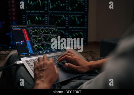 Nahaufnahme von Anlegern, die auf einem Laptop tippen, mit mehreren Finanz- und Kryptowährungsdiagrammen auf externen Bildschirmen, um den Echtzeitmarkt zu überwachen Stockfoto