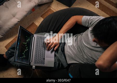 Top-Ansicht von Tradern, die von zu Hause aus arbeiten, Kryptowährungen oder Börsenanlagen auf einem Laptop handeln, Finanzdiagramme und -Daten in Echtzeit analysieren Stockfoto