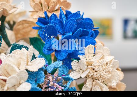 Eine Nahaufnahme eines Arrangements aus künstlichen Blumen, die aus gewebtem oder geripptem Material in lebhaften Blau-, Creme- und Beigetönen gefertigt sind. Die Stockfoto