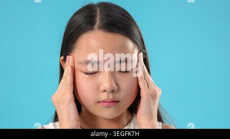 Junge müde asiatische Frau, die unter schmerzhaften Kopfschmerzen leidet und Schläfe hält Stockfoto