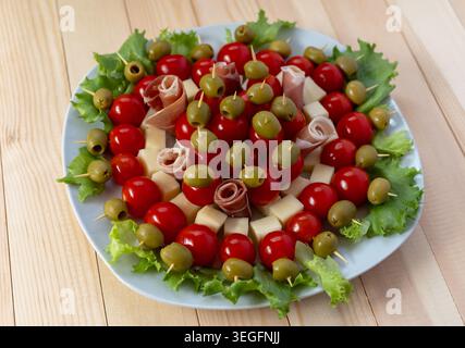 Ein professionelles Flachbild-Foto von einem runden weißen Teller voller festlicher Vorspeisen. Jeder Spieß enthält reife Kirschtomaten, grüne Oliven, che Stockfoto